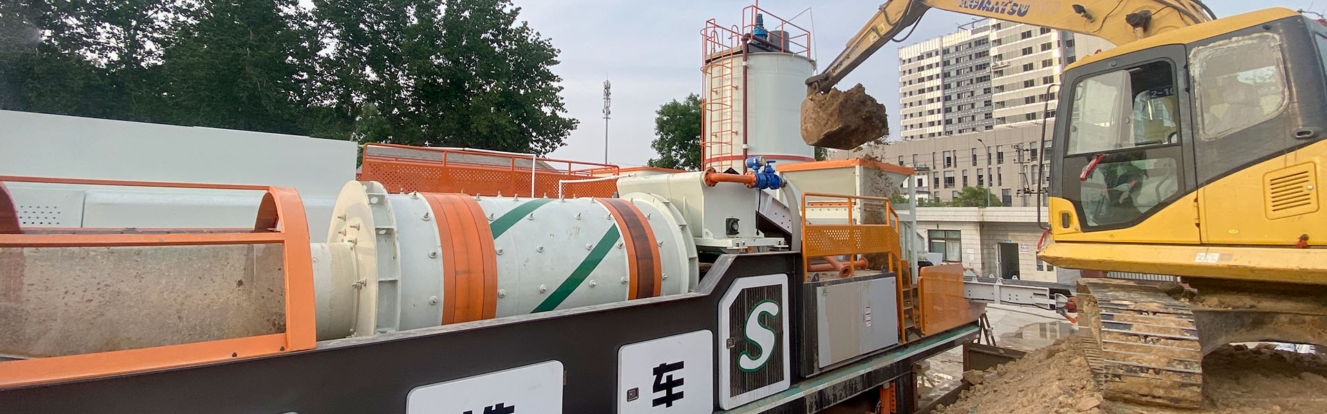 Rotary trommel screen on a soil treatment plant fed by an excavator